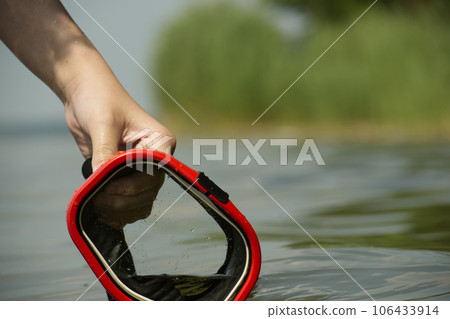 Hand holding a red and black mask in the water 106433914