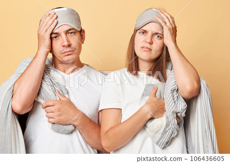 Oversleep couple man and woman in sleep eye mask wrapped in blanket isolated over beige background waking up early having headache need rest. Oversleep couple man and woman in sleep eye mask wrapped in blanket isolated over beige background waking up early having headache need rest. 106436605