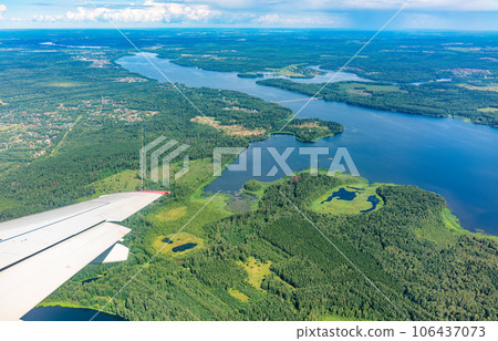 View of airplane wing, blue skies and green land and river during landing. Airplane window view. View of airplane wing, blue skies and green land and river during landing. Airplane window view. 106437073