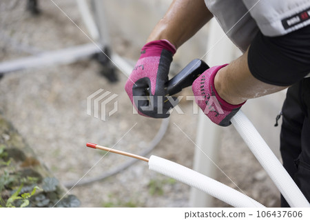 A male worker cuts a refrigerant pipe with a pipe cutter during air conditioner installation work A male worker cuts a refrigerant pipe with a pipe cutter during air conditioner installation work 106437606