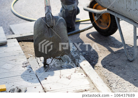 Worker lays foundation tiles of house. View of shovel with liquid cement. Builder repairing pavement 106437689