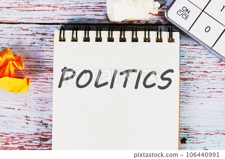 text of POLITICS written on a sheet of notebook lying on old vintage boards with a calculator and folded paper text of POLITICS written on a sheet of notebook lying on old vintage boards with a calculator and folded paper 106440991