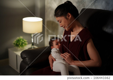 mother breastfeeding infant baby on sofa in the living room at night 106441082