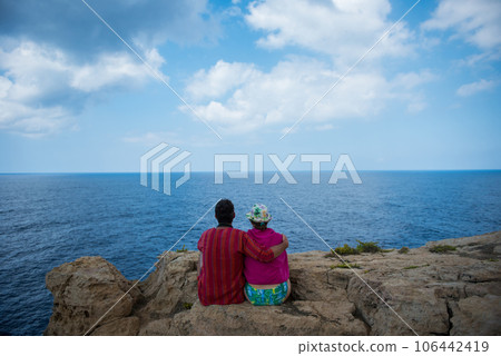 Romantic couple sitting on a cliff and admirig wonderful seascape 106442419