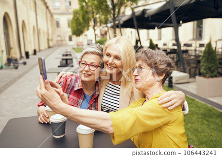 Mature smiling women friends taking selfie on phone while sitting in cafe terrace 106443241