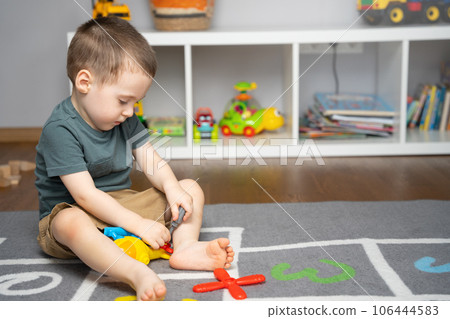 A little toddler boy 2.5 years is playing with a toy helicopter, assembling and disassembling it. Educational toys for kids. Children's room in home. Indoors A little toddler boy 2.5 years is playing with a toy helicopter, assembling and disassembling it. Educational toys for kids. Children's room in home. Indoors 106444583