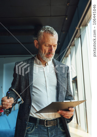 Focused businessman looking on documents and think how to solve problem while standing in office 106445846