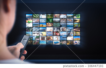 TV online. Multimedia streaming concept. Hand holding remote control. TV screen with lot of pictures. Person relaxing at home in evening 106447101