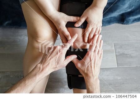 Therapist fitting a knee brace to female patient leg 106447504