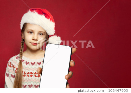 Adorable Christmas girl in Santa hat with smartphone on red background Adorable Christmas girl in Santa hat with smartphone on red background 106447903