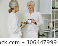 Two smiling middle aged female drinking coffee and chatting in modern office. 106447999