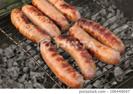 Grilled sausages. Cook man preparing grilling food bbq. Barbecue with smoke, flame outdoors. Tasty juicy german bratwurst. Charcoal kettle grill outside in backyard. Family summer vacation. Close-up 106448047
