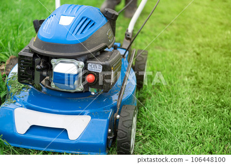 Lawn mower cutting grass. Small grass cuttings fly out of lawnmower. Grass clippings get spewed out of a mower pushed around by landscaper. CloseUp. Gardener working with mower machine. Mowing lawns Lawn mower cutting grass. Small grass cuttings fly out of lawnmower. Grass clippings get spewed out of a mower pushed around by landscaper. CloseUp. Gardener working with mower machine. Mowing lawns 106448100
