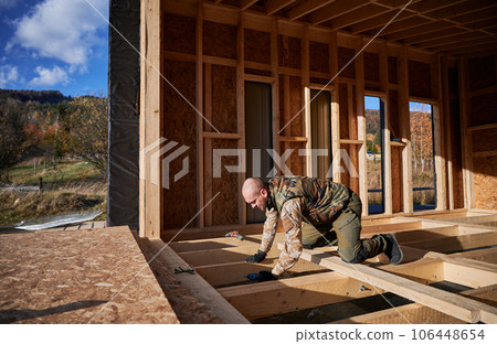 Male builder working with screwdriver inside of future cottage. Man worker building wooden frame house in the Scandinavian style barnhouse. Carpentry and construction concept. 106448654