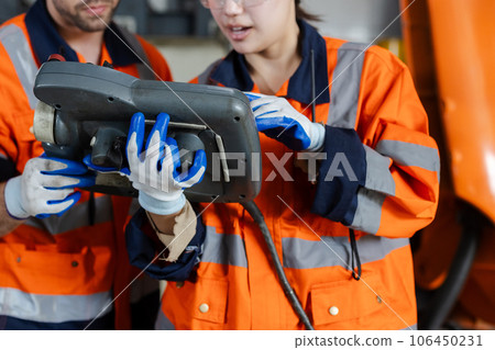 Close up woman engineer using remote robot controller operate standing at automation robot arms. 106450231