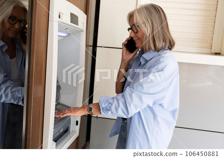 mature old woman talking on the phone and using an ATM mature old woman talking on the phone and using an ATM 106450881