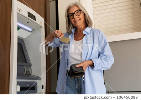 a mature adult woman went to an ATM on the street to insert a bank card to withdraw cash a mature adult woman went to an ATM on the street to insert a bank card to withdraw cash 106450889