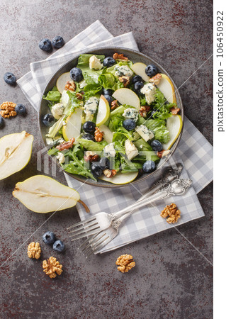 Autumn salad consisting of ripe pears, blueberries, blue cheese, lettuce and walnuts close-up in a plate. Vertical top view 106450922
