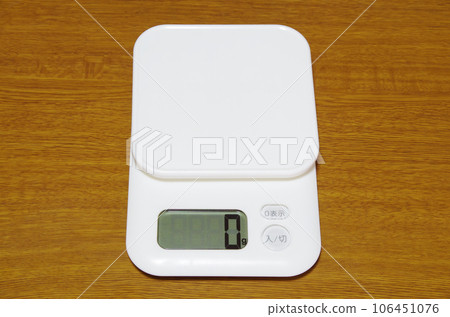 A digital balance scale showing 0g is placed on a woodgrain table. 106451076