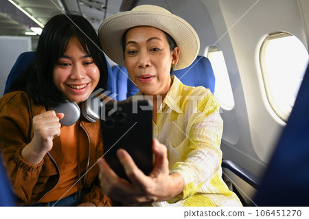 Happy middle aged woman and daughter sitting in passenger airplane and taking picture, waiting for airplane landing Happy middle aged woman and daughter sitting in passenger airplane and taking picture, waiting for airplane landing 106451270