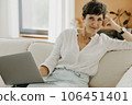 Portrait of middle aged woman sitting on couch with laptop. 106451401