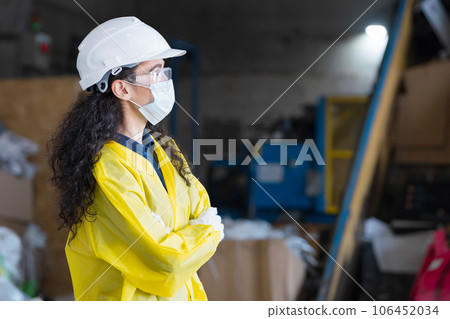 Woman in helmet watches workers sorting waste at plant 106452034