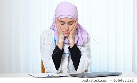 Muslim woman in doctor suit works with tired expression Muslim woman in doctor suit works with tired expression 106452188
