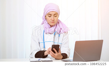 Practitioner in hijab types messages to patient on phone Practitioner in hijab types messages to patient on phone 106452225