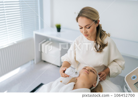 High-angle view of blonde young woman getting SMAS lifting procedure on cheek in cosmetology salon with light interior. Concept of non-surgery cosmetology, professional skincare, beauty treatment. 106452700