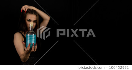 Copy space. Banner, leaflet. For halloween, a woman witch holds out a bottle with a glowing potion on a black background. Witch in a black dress with long black hair for halloween. 106452951