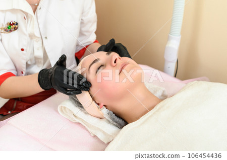Portrait of a happy girl getting a facial massage in a spa salon 106454436