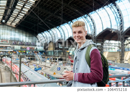 Portrait of smiling young guy with backpack smartphone at train station Portrait of smiling young guy with backpack smartphone at train station 106455218