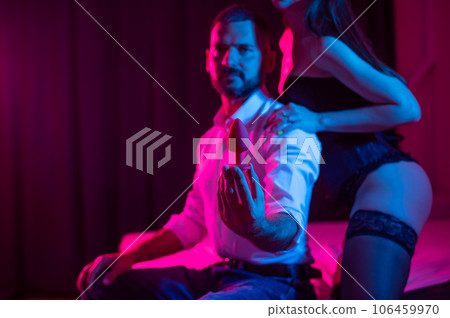 A couple of lovers use an anal plug in the bedroom in neon light. 106459970