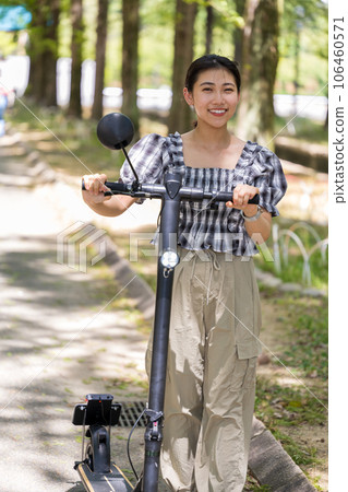 A young and cute woman taking a walk on an electric kickboard in the refreshing sunlight filtering through the trees | Electric kickboard image A young and cute woman taking a walk on an electric kickboard in the refreshing sunlight filtering through the trees | Electric kickboard image 106460571