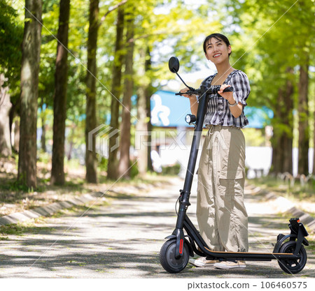 A young and cute woman taking a walk on an electric kickboard in the refreshing sunlight filtering through the trees | Electric kickboard image 106460575