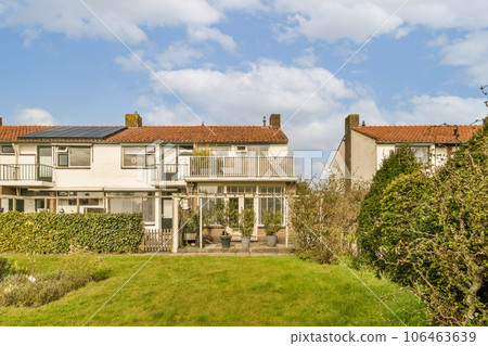 a house with solar panels on the roof and green grass in front yard, surrounded by trees and bushes against blue sky 106463639