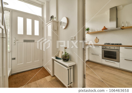 a white kitchen with wood flooring and an open door that leads to the living room on the other side a white kitchen with wood flooring and an open door that leads to the living room on the other side 106463658