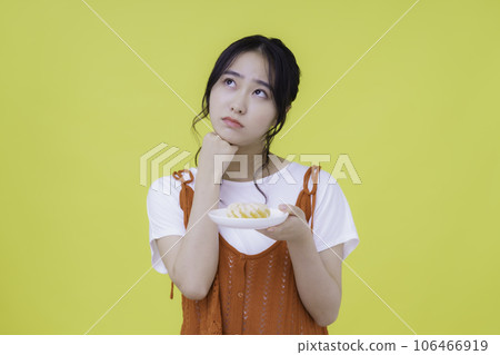 Portrait of a troubled young woman with donut in hand against yellow background 106466919