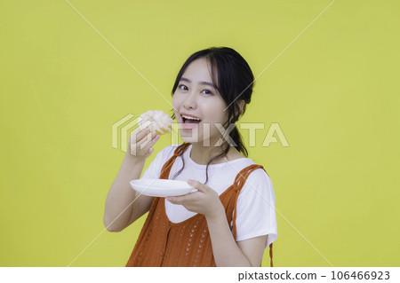 Portrait of a troubled young woman with donut in hand against yellow background 106466923