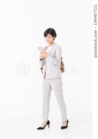 A business woman walking with a smartphone against a white background 106467722