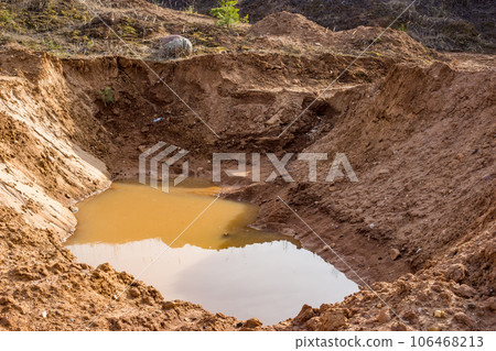 A large hole dug in sandy soil and flooded with water 106468213