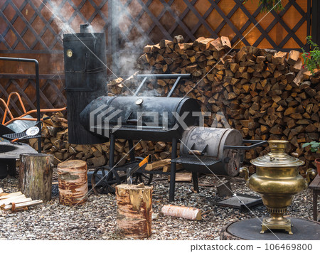 Big iron smokehouse with firewood stands on the courtyard. On the smokehouse, you can smoke various healthy foods. Small business smoking concept. Big iron smokehouse with firewood stands on the courtyard. On the smokehouse, you can smoke various healthy foods. Small business smoking concept. 106469800