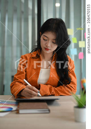 Concentrated Asian female artist drawing something on digital tablet working on new design project at modern creative office Concentrated Asian female artist drawing something on digital tablet working on new design project at modern creative office 106470555