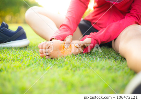 Girl sitting on green grass in the park. Foot pain from the wrong exercise .Symptoms of peripheral neuropathy. Most symptoms are numbness in the fingertips and foot. sun set light background. 106472121