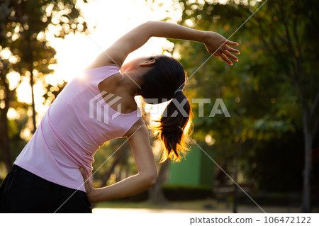 Young female stretching before fitness training session at the park. on the blue running track , green tree bokeh and green grass background at sunset. Young female stretching before fitness training session at the park. on the blue running track , green tree bokeh and green grass background at sunset. 106472122
