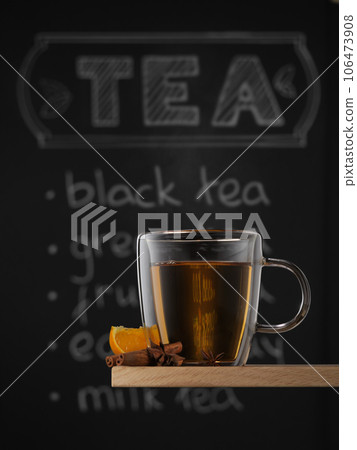 Clear glass mug with hot black tea, orange, cinnamone and anise against chalkboard background with tea written on it. 106473908