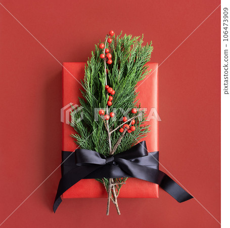 Red gift box with thuja, berries and black ribbon on a red background Red gift box with thuja, berries and black ribbon on a red background 106473909