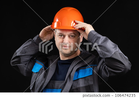 A young man construction worker in a safety helmet and work uniform on a black background A young man construction worker in a safety helmet and work uniform on a black background 106474235