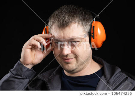 A man in earmuffs, glasses and overalls on a black background. 106474236