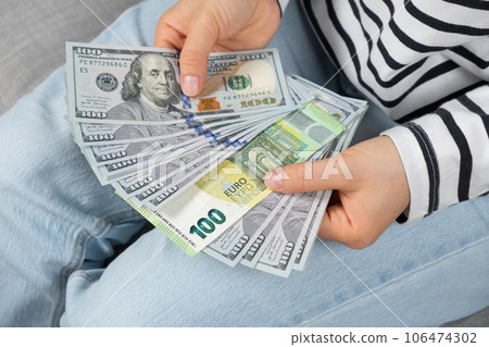 A 100 euro bill among many 100 dollar bills in the hands of a person 106474302